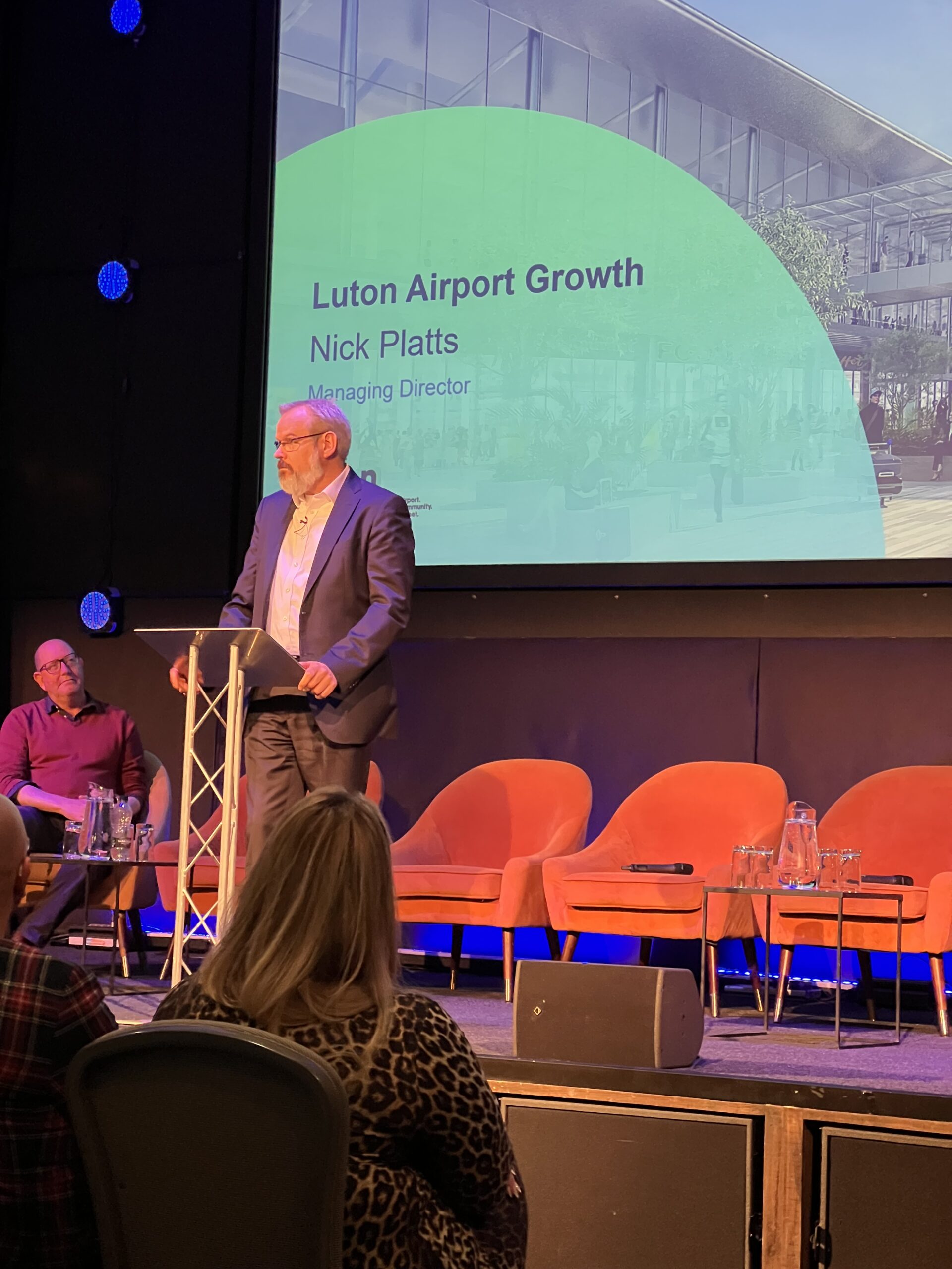 Nick Platts of Luton Rising speaking at the lectern in front of a Luton Airport Growth slide.