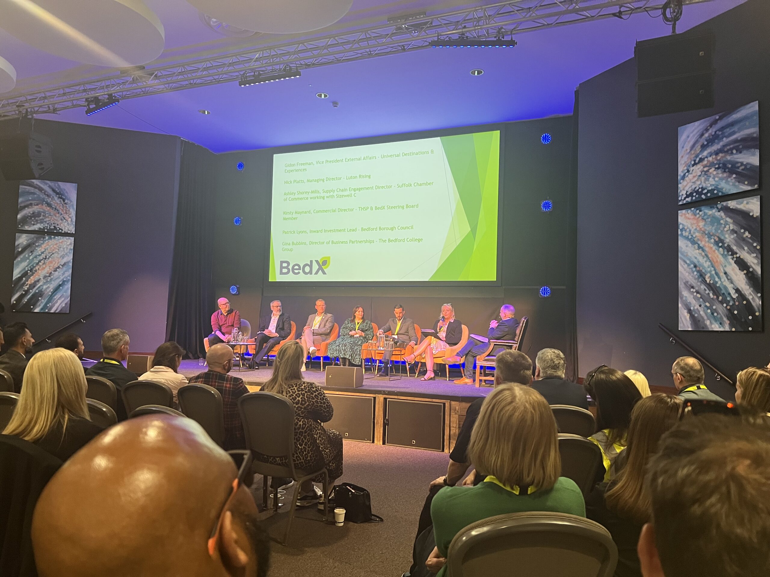 The BedX panel on stage at King's House, Bedford, with the speaker list projected behind them.