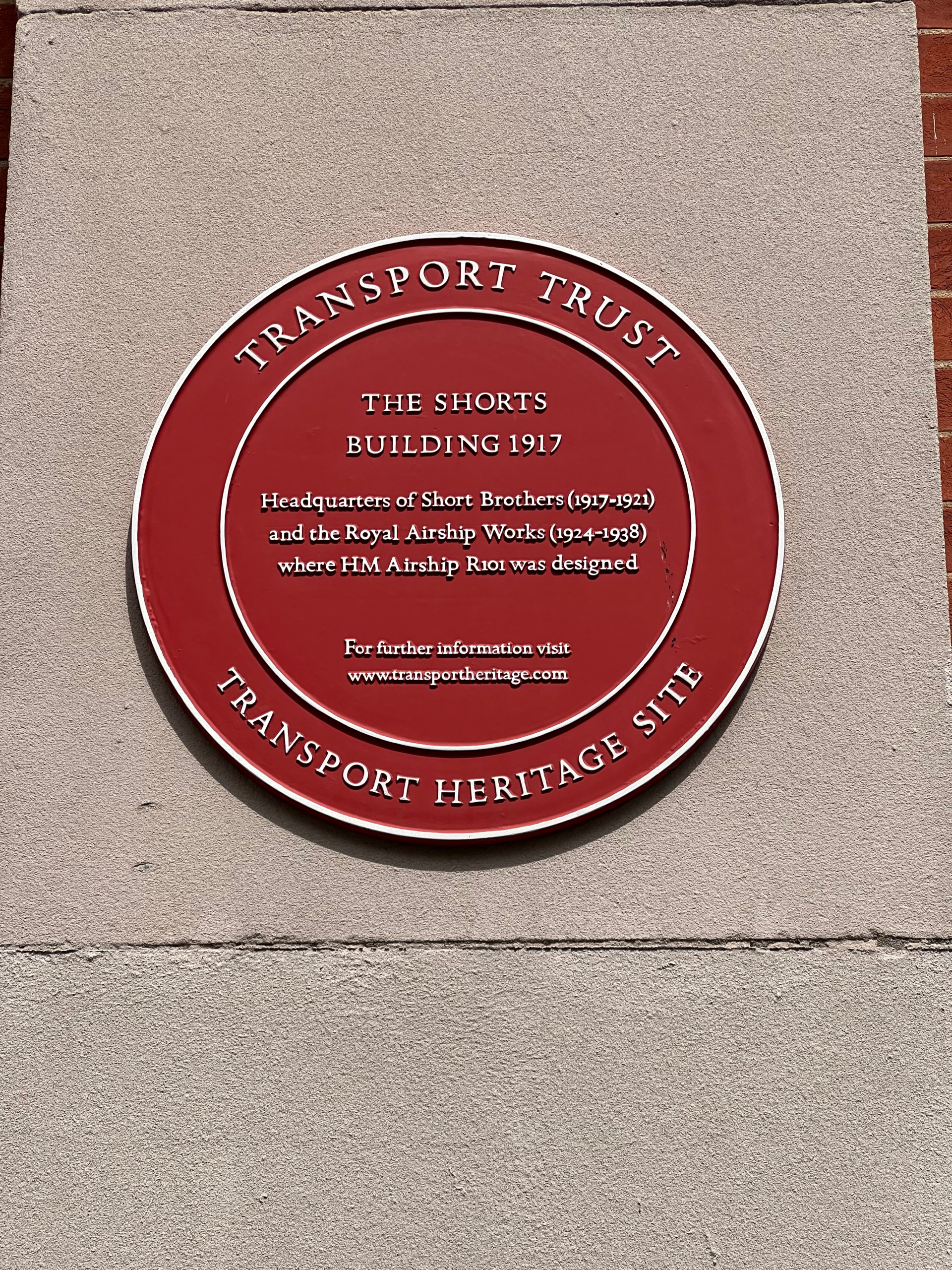 The red Transport Trust heritage plaque on the Shorts Building, recording it as the headquarters of Short Brothers and the Royal Airship Works, where HM Airship R101 was designed