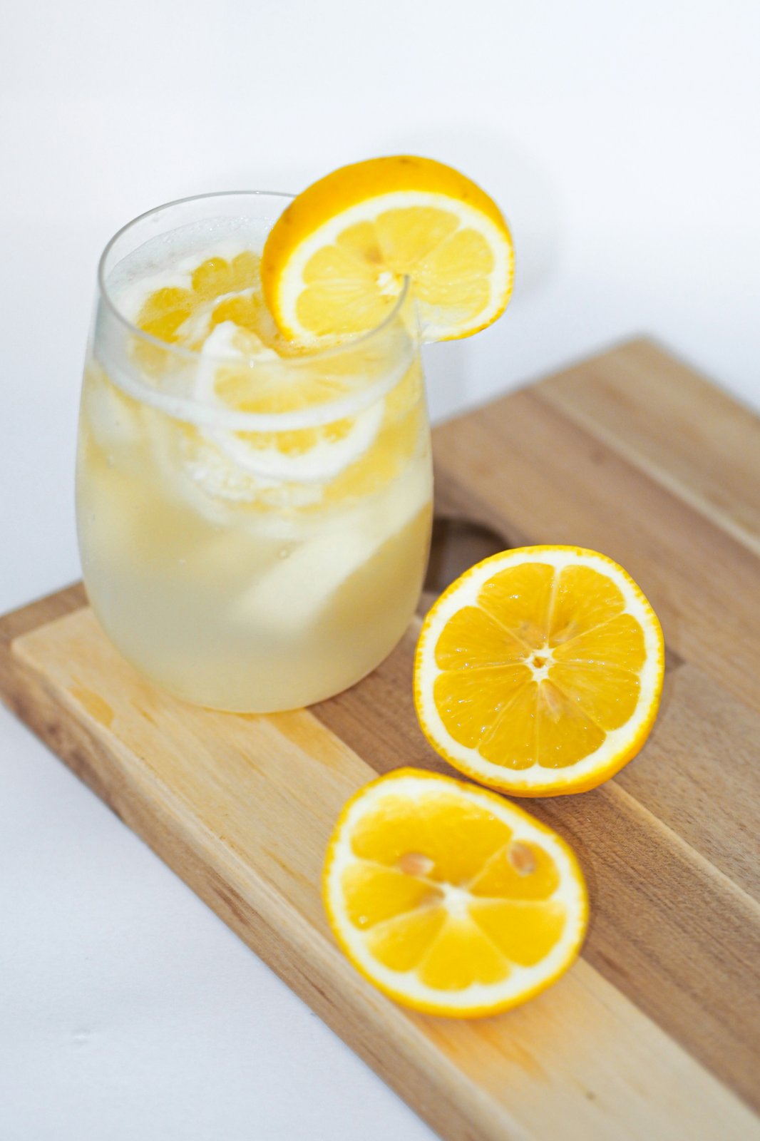 A glass of homemade lemonade with lemon slices on a wooden board